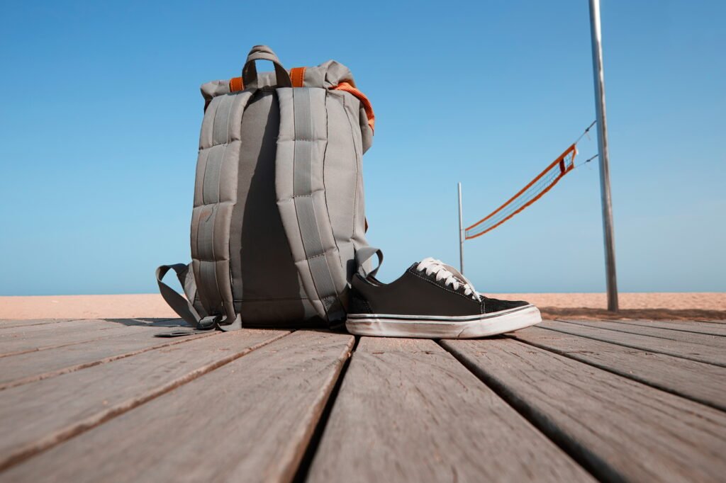 Summer travel concept. Backpack and sneakers are on the wooden desk near the beach
