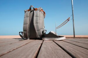 Summer travel concept. Backpack and sneakers are on the wooden desk near the beach